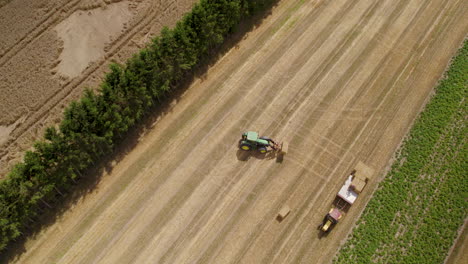 Ein-Landwirtschaftlicher-Traktor-Auf-Einem-Feld,-Der-Einen-Quadratischen-Heuballen-Trägt,-Der-Ihn-Zum-Transport-Auf-Einen-Anhänger-Lädt