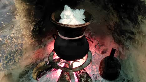 Moroccan-couscous-cooking-on-a-couscoussier-steamer-to-steam-it
on-a-wooden-fire-in-a-fireplace,-smoke-and-flame-surround-the-pot-1