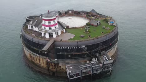 Aerial-drone-flight-around-the-Solent-Fort-in-The-Isle-of-Wight-showing-the-gardens-and-Red-and-White-Lighthouse-in-the-English-Channel