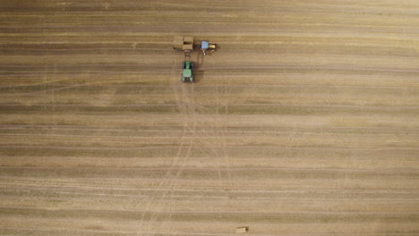 Aerial-top-down-of-farmer-in-harvester-machinery-cutting-on-wheat-field-and-loading-on-tractor-trailer