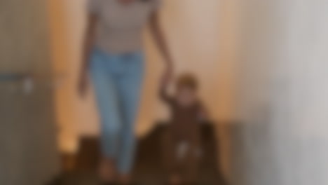 Blurred-shot-of-a-mother-helping-her-toddler-son-walking-up-the-stairs,-motherhood-and-parenting-concept