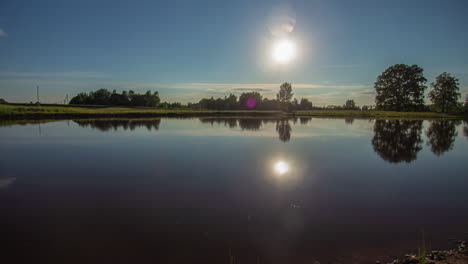 Statische-Aufnahme-Eines-Wunderschönen-Sommersonnenuntergangs-Im-Zeitraffer-über-Einem-See,-Umgeben-Von-Ländlicher-Landschaft