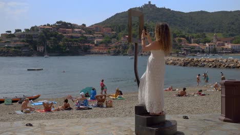 Woman-walking-towards-the-picture-frame-to-take-a-picture-of-the-beach-in-Collioure,-France
