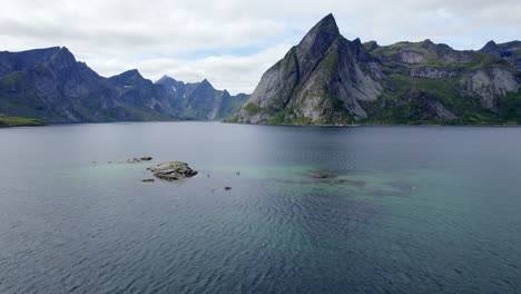 Aerial-forwarding-shot-of-scenic-mountains-in-Reinefjorden-on-Lofoten-Island-with-Stand-up-Paddler-on-a-nice-summer-day