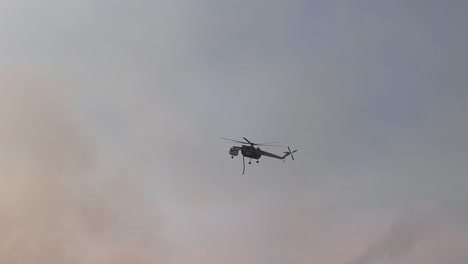 Air-crane-copter-flying-over-woods-and-hills,-dropping-water-on-burning-nature