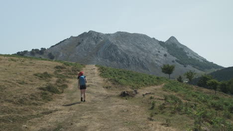 Rear-view-of-a-young-woman-trekking-to-the-limestone-mountain-of-Anboto-in-Spain's-Western-Basque-Country-while-carrying-a-blue-bag