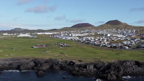 Beautiful-green-grass-golf-club-course-on-volcanic-island-with-small-town,-aerial
