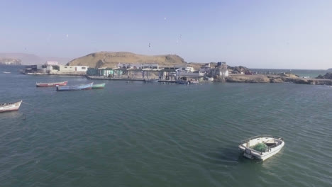 Zoom-out-with-drone-of-the-sea-in-a-Peruvian-port-with-boats-floating-and-seagulls-flying