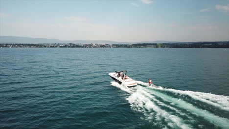 Aerial-drone-view-of-a-boat-sailing-on-Lake-Geneva,-an-athlete-is-wakesurfing,-Switzerland