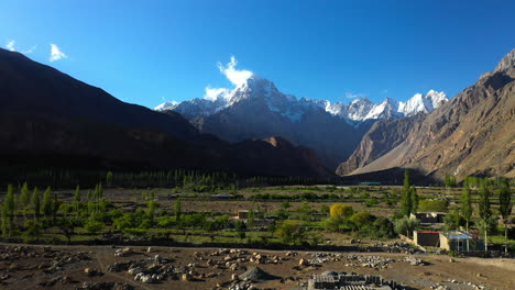 Cinematic-drone-shot-of-the-sun-shining-in-the-valley,-Passu-Cones-in-Hunza-Pakistan,-snow-covered-mountain-peaks-with-steep-cliffs,-moving-towards-mountains-from-low-level