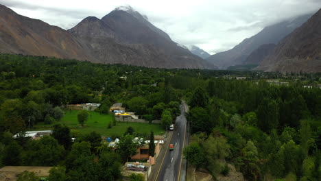Dramatic-drone-shot-following-a-tuk-tuk-on-the-Karakoram-Highway-Pakistan-in-a-small-town-or-village,-wide-chasing-aerial-shot