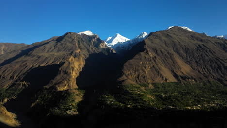 Filmische-Drohnenaufnahme-Der-Sonne,-Die-Im-Tal-Scheint,-Passu-Kegel-In-Hunza-Pakistan,-Schneebedeckte-Berggipfel-Mit-Steilen-Klippen,-Rotierende-Breite-Luftaufnahme