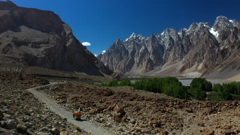 Cinematic-drone-shot-of-a-tuk-tuk-on-a-gravel-path-on-the-Karakoram-Highway-Pakistan-with-the-passu-cones-in-the-distance