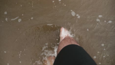 A-man-walking-along-a-beach-as-the-water-laps-at-his-feet