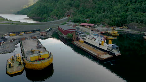 Industrial-Harbour-In-Fjord-In-Rural-Landscape-With-Ferry-And-Shipping-Vessels-Docked-At-Daytime