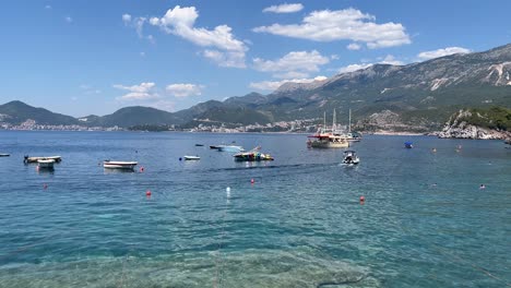 Still-water-surrounding-the-island-of-Sveti-Stefan-in-Montenegro-on-a-beautifully-sunny-day-with-the-high-mountains-over-the-water-filled-with-boats