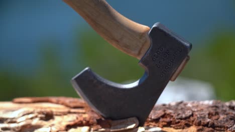 Closeup-of-hatchet-inserted-to-firewood-log---camera-slowly-moving-upwards-from-steel-blade-to-shaft-with-blurred-shallow-depth-background---Sunny-day-handheld
