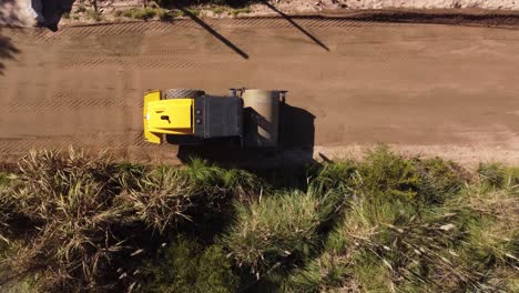 Aerial-top-down-shot-of-yellow-rolling-leveling-machine-working-on-construction-site-road-on-sunny-day