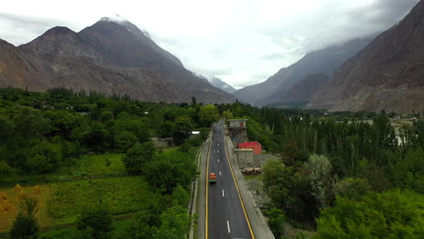 Drone-shot-following-a-tuk-tuk-on-the-Karakoram-Highway-Pakistan-in-a-small-town-or-village,-chasing-aerial-shot