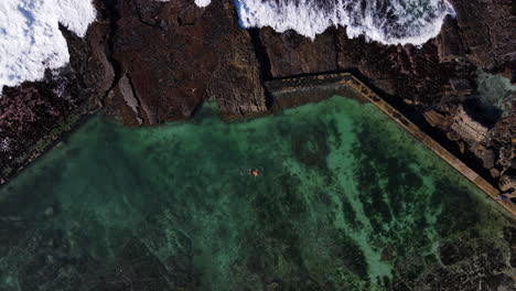 Man-swims-in-marine-tidal-pool-on-rocky-coastline