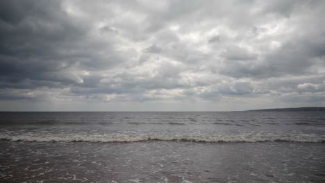 A-view-from-the-beach-as-waves-lap-at-the-shore-with-a-dramatic,-overcast-skyline