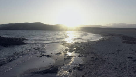Schöne-Aufnahme-Der-Küste-Eines-Strandes-Während-Des-Sonnenuntergangs,-Wenn-Die-Wellen-Gegen-Die-Felsen-Schlagen-Und-Die-Sonne-Das-Meer-Erleuchtet
