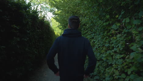 Unrecognizable-man-wearing-a-black-hoodie-seen-from-the-back-while-walking-in-the-park-after-exercising,-tracking-shot