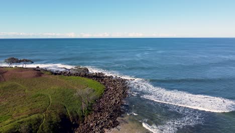 Drone-aerial-pan-shot-of-surfers-line-up-reef-rocky-landscape-scenery-nature-island-Yamba-Angourie-headland-NSW-North-Coast-Australia-4K