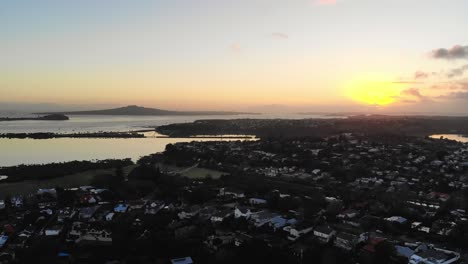 Golden-hour-aerial-over-Auckland-neighbourhood,-Rangitoto-island-background