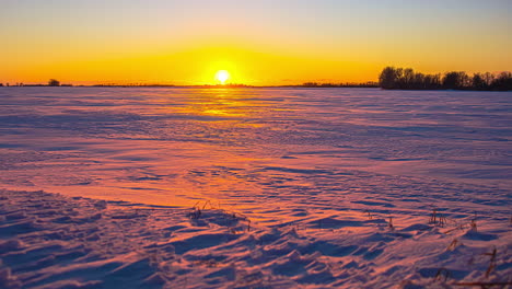 Bright-yellow-sunset-time-lapse-over-a-field-of-snow---dusk-falls-on-the-wide-angle-winter-scene
