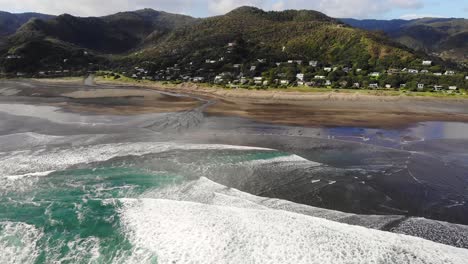 Stream-flowing-into-Tasman-Sea-at-scenic-black-sand-Piha-beach,-aerial