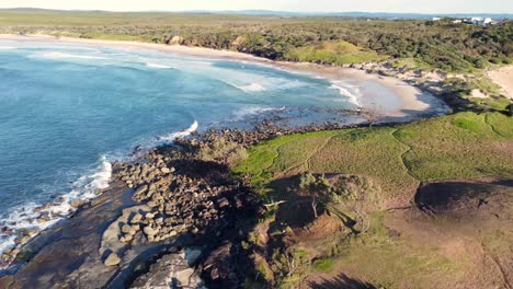 Drone-aerial-pan-shot-of-Island-reef-rocky-beach-surf-spot-beautiful-nature-view-bushland-headland-Yamba-Angourie-North-Coast-NSW-Australia-4K