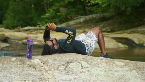 A-man-lays-down-on-a-giant-rock-in-the-middle-of-a-lush-green-forest