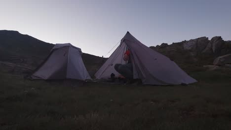Early-morning-sunrise-tent-opening-from-the-inside-and-young-hiker-getting-out-with-red-down-jacket