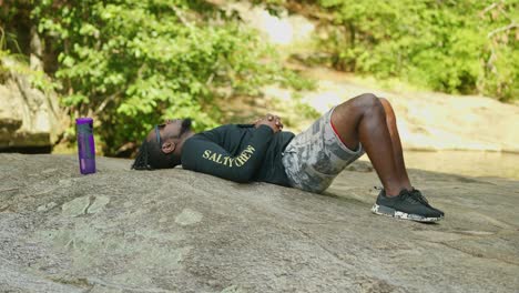 A-man-lays-down-and-relaxes-on-a-giant-rock-in-the-middle-of-the-woods-on-a-bright-sunny-day