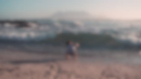 Blurred-shot-of-young-child-getting-knocked-down-by-sea-waves-on-the-beach-and-being-rescued-by-his-mother