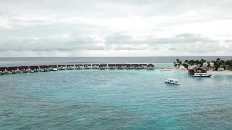 Drone-shot-of-water-villas,-yachts-and-an-Island-with-palms-in-a-Maldives-resort