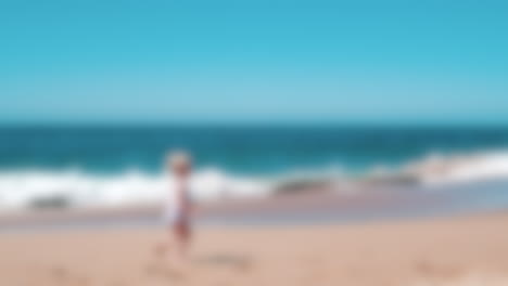 Blurred-shot-background-of-mother-and-daughter-running-on-the-beach-next-to-the-sea-waves-during-a-sunny-day,-vacations-concept