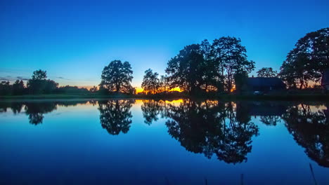 Static-shot-of-sun-setting-in-timelapse-over-clear-blue-sky-over-lakeside-cottage-during-evening-time