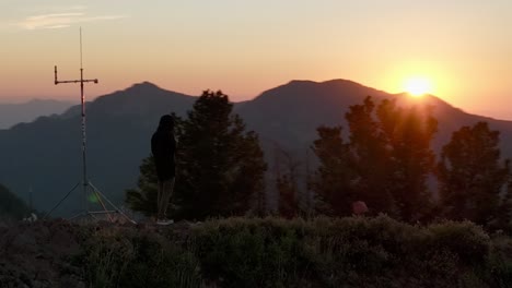 Aerial-orbiting-hiker-standing-on-mountain-peak-at-sunset-in-the-backcountry