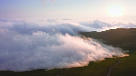 Sunset-In-Foggy-Mountains,-Dense-Clouds-Creeping-Over-Slanted-Plateau,-Aerial-Shot-From-Drone