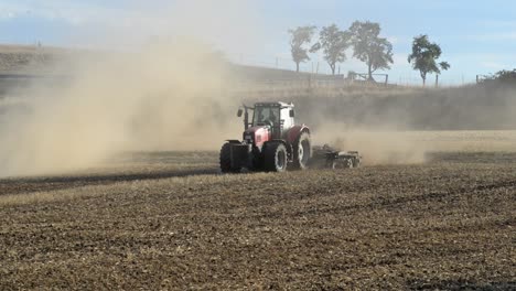 Red-tractor-turning-while-plowing-a-dry-dusty-field-to-prepare-it-for-sowing