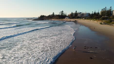 Drone-aerial-pan-shot-of-surfer-walking-on-beach-Town-rural-coastal-lifestyle-tourism-travel-views-Port-Macquarie-NSW-Mid-North-Coast-Australia