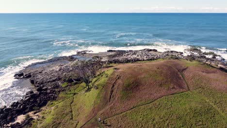 Drone-aerial-pan-shot-view-landscape-nature-scenery-couple-people-walking-trail-beach-ocean-reef-rocky-Yamba-Angourie-North-Coast-headland-NSW-Australia-4K