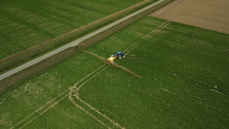 Tractor-with-trailed-sprayer-follows-the-tracks-in-a-field-and-turns-to-the-right,-aerial-view