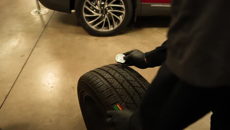 Mechanic-checking-tire-tread-depth,-panning-shot