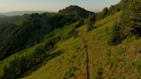 Antenne-über-Der-Bergkette-Im-Hinterland,-Während-Zwei-Biker-Bei-Sonnenuntergang-Den-Trail-Hinunterfahren-1