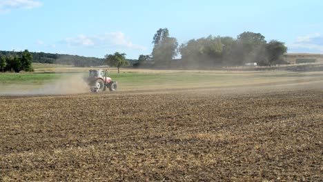 Empty,-dry-field-being-plowed-by-a-small-tractor-that-swirls-up-enormous-amounts-of-dirt-and-dust