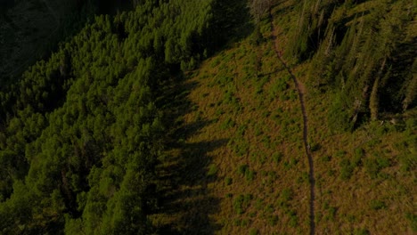 Aerial-over-backcountry-mountain-range-as-two-bikers-bike-down-trail-at-sunset