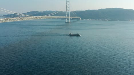 Barco-Navegando-Más-Allá-Del-Puente-Akashi-Kaikyo-Con-La-Isla-Awaji-En-La-Distancia